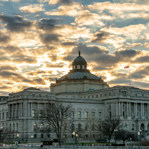 U.S. Library of Congress building with large dome. Clouds and sun peeking through visible above and behind the building.